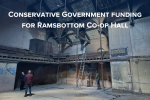  The image shows the Ramsbottom Co-op Hall's interior, characterized by vintage architectural details and a balcony, in need of restoration. Visible signs of wear, such as peeling paint, indicate neglect. People in the hall suggest a planning or assessment activity. The text highlights Conservative Government funding for the hall's renewal. Generated automatically.